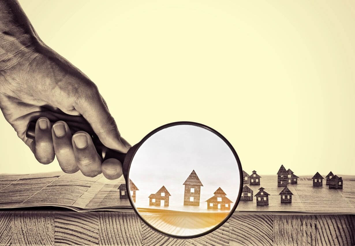 A hand holding a magnifying glass over a row of houses.